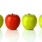 green apple with the red one standing out from the crowd - over a white background with reflection